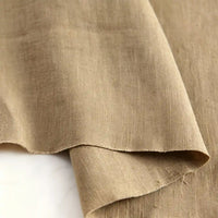 A close-up photo of Longan Craft’s Pure Color 100 Linen Fabric By The Yard, highlighting the medium weight linen’s textured natural weave, with the edge of this 100% linen clothing material gently curling over a lighter background.