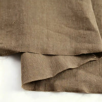 A close-up of Longan Craft’s Pure Color 100 Linen Fabric By The Yard, neatly folded on a light surface, highlights the natural texture and visible weave pattern of this medium weight, comfy linen fabric—ideal for casual wear.
