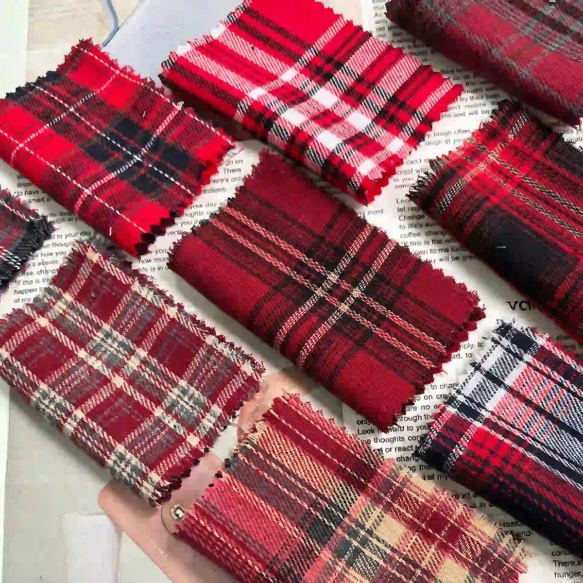 Several pieces of the Red Checked Cotton Flannel Fabric by Longan Craft, featuring various Scottish-style plaid patterns, are neatly arranged atop an open magazine or newspaper.