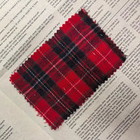 A piece of Longan Craft’s Red Checked Cotton Flannel Fabric By The Yard, featuring a Scottish-style single-sided brushed flannel material with frayed edges, is laid atop a newspaper with printed text.
