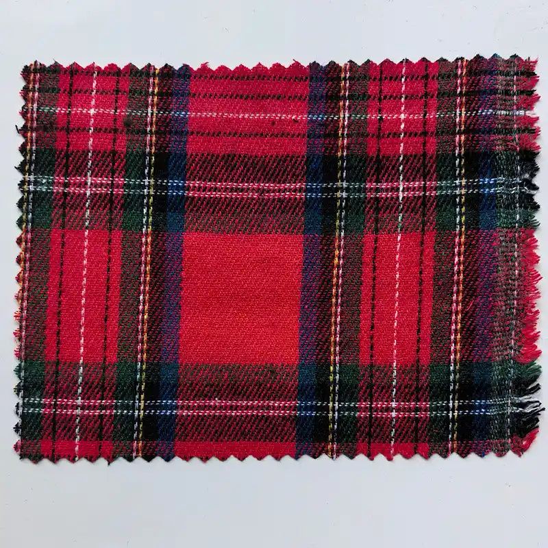 A rectangular sample of Longan Craft’s Red Checked Cotton Flannel Fabric By The Yard—featuring a classic Scottish-style pattern in red with black, white, yellow, and green lines—is shown lying flat on a light background with zigzag-cut edges.