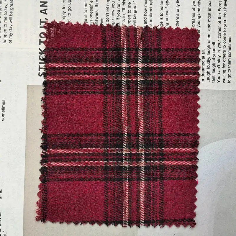 A rectangular swatch of Longan Craft’s Red Checked Cotton Flannel Fabric By The Yard, featuring a Scottish style single-sided brushed finish and vintage fall plaid pattern with serrated edges, is placed on top of a newspaper page.
