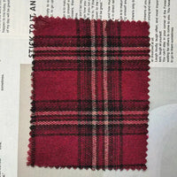 A rectangular swatch of Longan Craft’s Red Checked Cotton Flannel Fabric By The Yard, featuring a Scottish style single-sided brushed finish and vintage fall plaid pattern with serrated edges, is placed on top of a newspaper page.