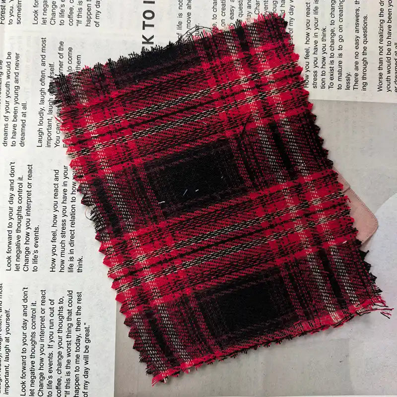 A swatch of Longan Craft Red Checked Cotton Flannel Fabric By The Yard, a Scottish style single-sided brushed flannel material with zigzag-cut edges, rests atop a page of printed text.