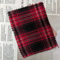 A swatch of Longan Craft Red Checked Cotton Flannel Fabric By The Yard, a Scottish style single-sided brushed flannel material with zigzag-cut edges, rests atop a page of printed text.