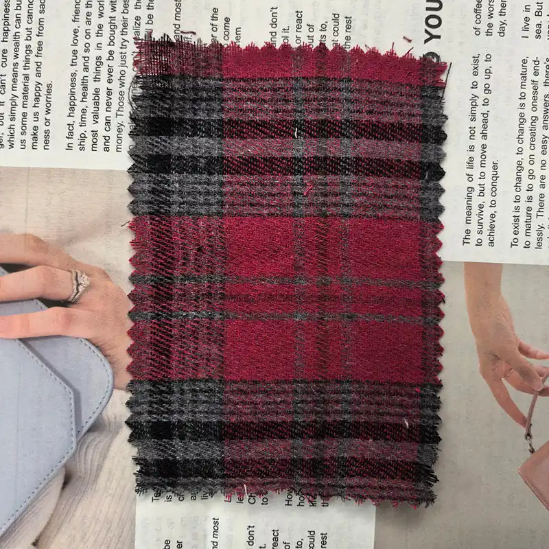 A piece of Longan Craft Red Checked Cotton Flannel Fabric By The Yard, featuring a vintage Scottish style with single sided brushed flannel material, rests atop a newspaper page, partially concealing images of hands holding bags.