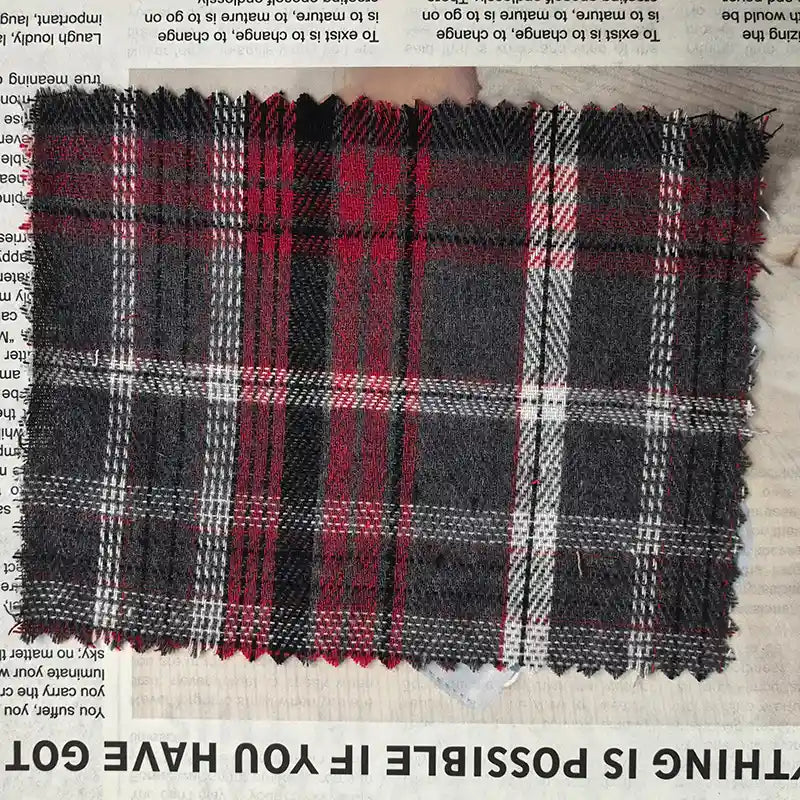 A rectangular piece of Longan Craft Red Checked Cotton Flannel Fabric By The Yard, a Scottish style single sided brushed flannel material in black, white, and red, is placed on top of a newspaper with some text visible along the edges.