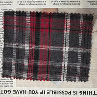 A rectangular piece of Longan Craft Red Checked Cotton Flannel Fabric By The Yard, a Scottish style single sided brushed flannel material in black, white, and red, is placed on top of a newspaper with some text visible along the edges.
