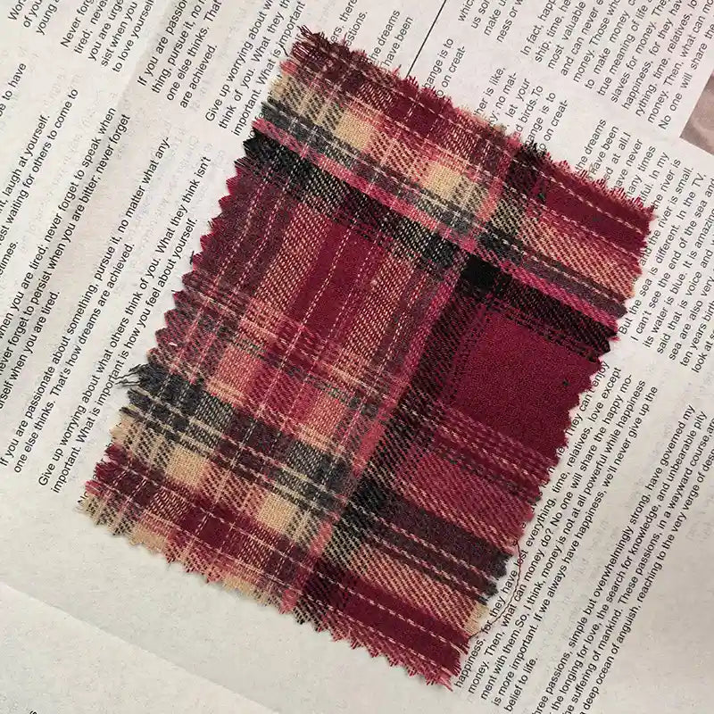 A rectangular piece of Longan Craft Red Checked Cotton Flannel Fabric By The Yard, featuring Scottish style single-sided brushed flannel in red, black, and beige plaid with frayed edges, is laid on top of an open newspaper with visible text.