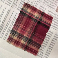 A rectangular piece of Longan Craft Red Checked Cotton Flannel Fabric By The Yard, featuring Scottish style single-sided brushed flannel in red, black, and beige plaid with frayed edges, is laid on top of an open newspaper with visible text.