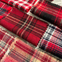 Close-up of several rectangular fabric swatches in red, black, and white plaid patterns—including the Red Checked Cotton Flannel Fabric By The Yard from Longan Craft—arranged on a sheet of printed text. The Scottish style single-sided brushed flannel material features pinked edges with a distinctive zigzag cut.
