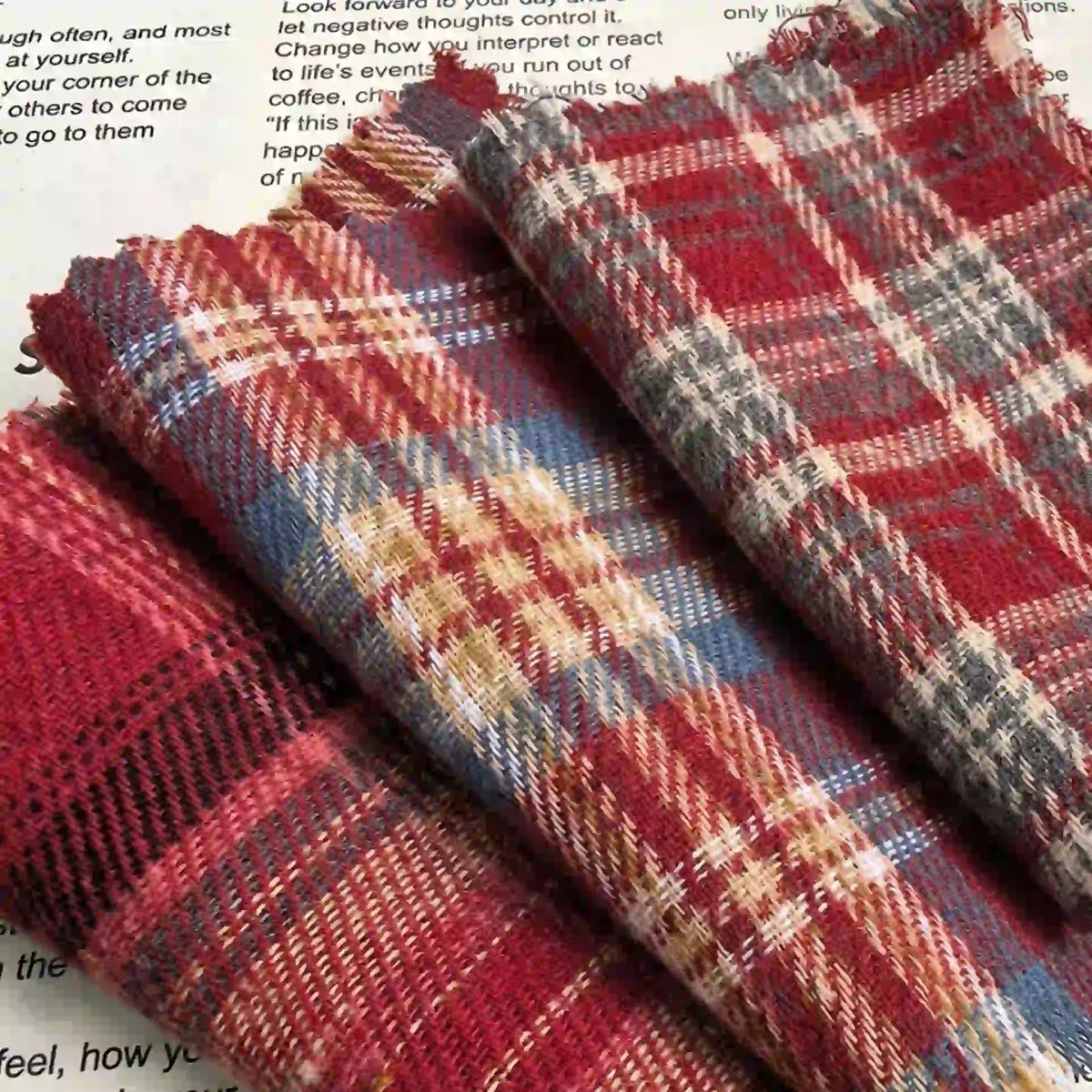 Three folded pieces of the Longan Craft Red Checked Cotton Flannel Fabric By The Yard, featuring a Scottish style with blue and yellow accents, rest on a white surface with black text partially visible underneath.