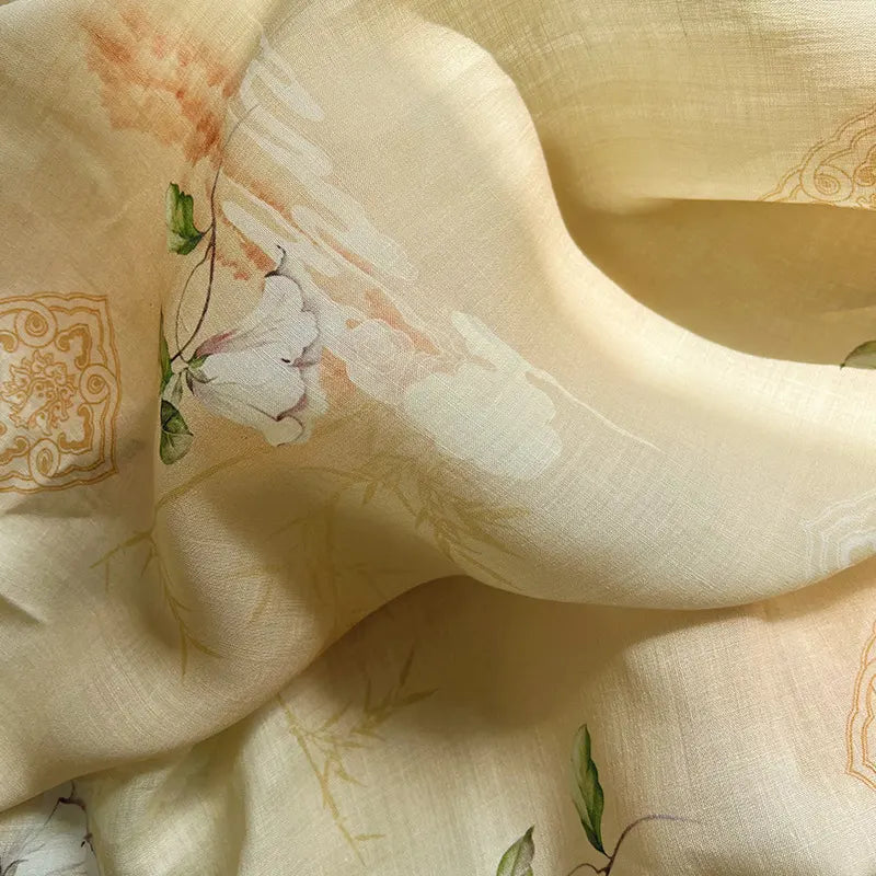 A close-up of the Retro Botanical Printed Ramie Fabric by Longan Craft, showcasing lightweight chinoiserie floral print ramie material in a soft, flowing light yellow texture. The fabric features delicate white, green, and peach botanical patterns with subtle ornate gold accents—perfect for blouses.