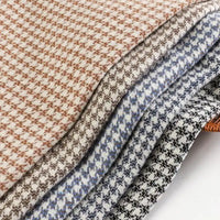 Four pieces of Longan Craft’s Retro Houndstooth Jacquard Tweed Fabric by the Yard, featuring a timeless houndstooth pattern in brown, beige, blue, and black tones, are neatly stacked on a white surface. Made from a wool polyester blend material, this vintage-inspired tweed fabric is ideal for crafting coats and suits that combine classic elegance with contemporary style.