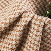 Close-up of the Retro Houndstooth Jacquard Tweed Fabric by the yard from Longan Craft, featuring a beige and brown vintage-inspired pattern in a soft wool-polyester blend. A small plant with green leaves is partially visible on the right side.