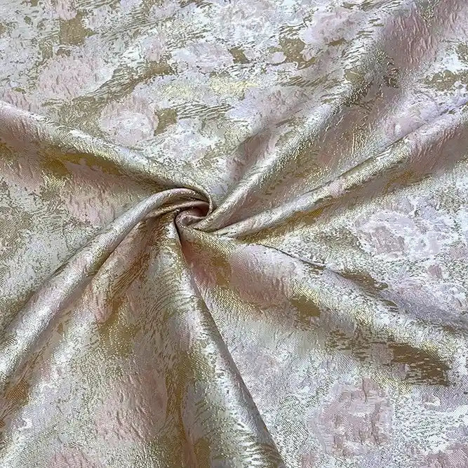 A close-up of Longan Craft's Rose Jacquard Brocade Fabric By The Yard in light gold and pale pink, arranged in soft folds with a spiral twist. This retro formal dress material features a golden metallic floral pattern and textured shimmer.