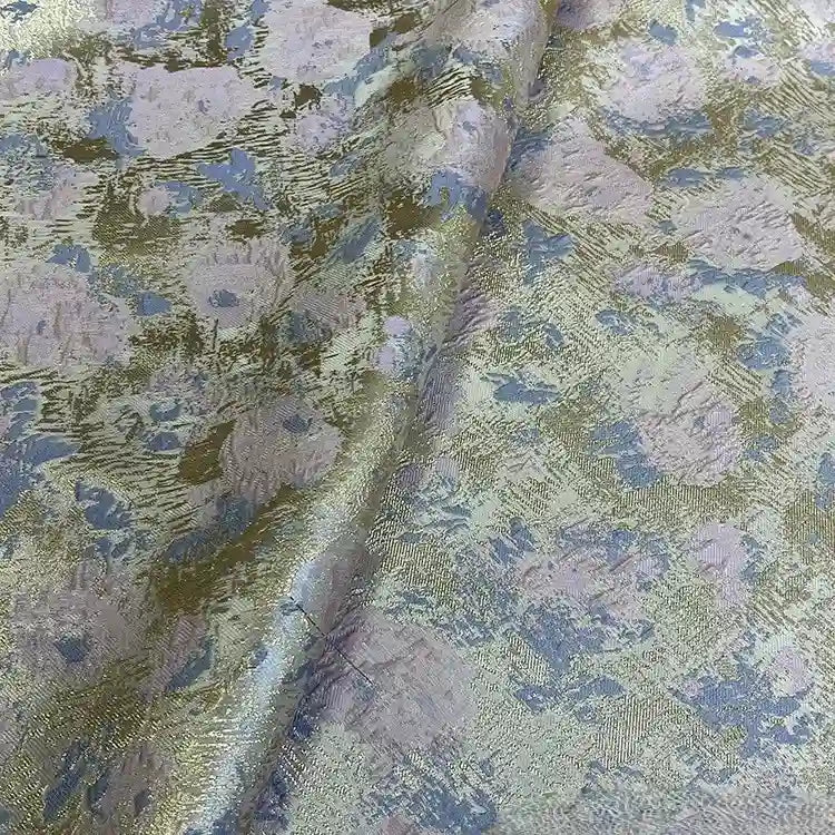 A close-up of Longan Craft’s Rose Jacquard Brocade Fabric By The Yard shows its golden metallic floral pattern in pastel blue and purple. This soft, slightly wrinkled retro brocade is perfect for upholstery or formal dresses.