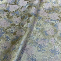 A close-up of Longan Craft’s Rose Jacquard Brocade Fabric By The Yard shows its golden metallic floral pattern in pastel blue and purple. This soft, slightly wrinkled retro brocade is perfect for upholstery or formal dresses.