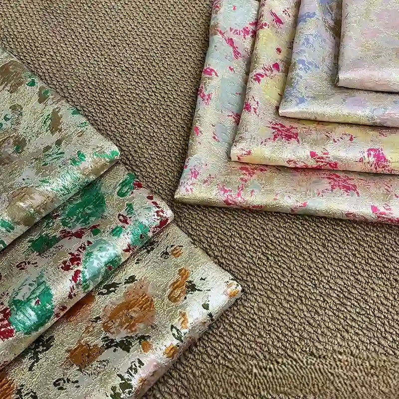 Multiple folded pieces of Rose Jacquard Brocade Fabric by Longan Craft, featuring golden metallic floral patterns in vibrant hues, are arranged on a brown surface, highlighting the retro elegance of this fabric by the yard for formal dresses.