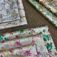 Rose Jacquard Brocade Fabric by Longan Craft is displayed on a brown carpet, featuring golden metallic floral patterns in green, red, orange, blue, and silver tones—ideal retro brocade material for formal dresses by the yard.