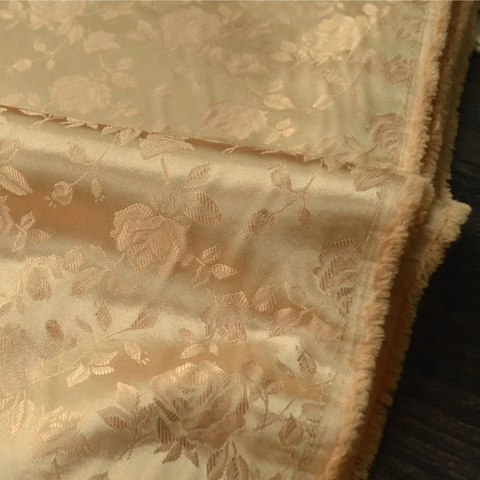 Longan Craft’s Rose Jacquard Satin Fabric By The Yard, a colorful polyester floral jacquard with a soft, slightly shiny finish, is displayed folded on dark wood—perfect satin textile for costumes.