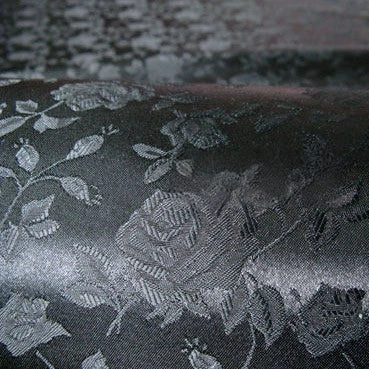 Close-up of Longan Craft’s Rose Jacquard Satin Fabric By The Yard—a colorful polyester satin with an embossed floral pattern and shiny, textured finish, ideal for costumes. Light reflects off its intricate rose and leaf design.