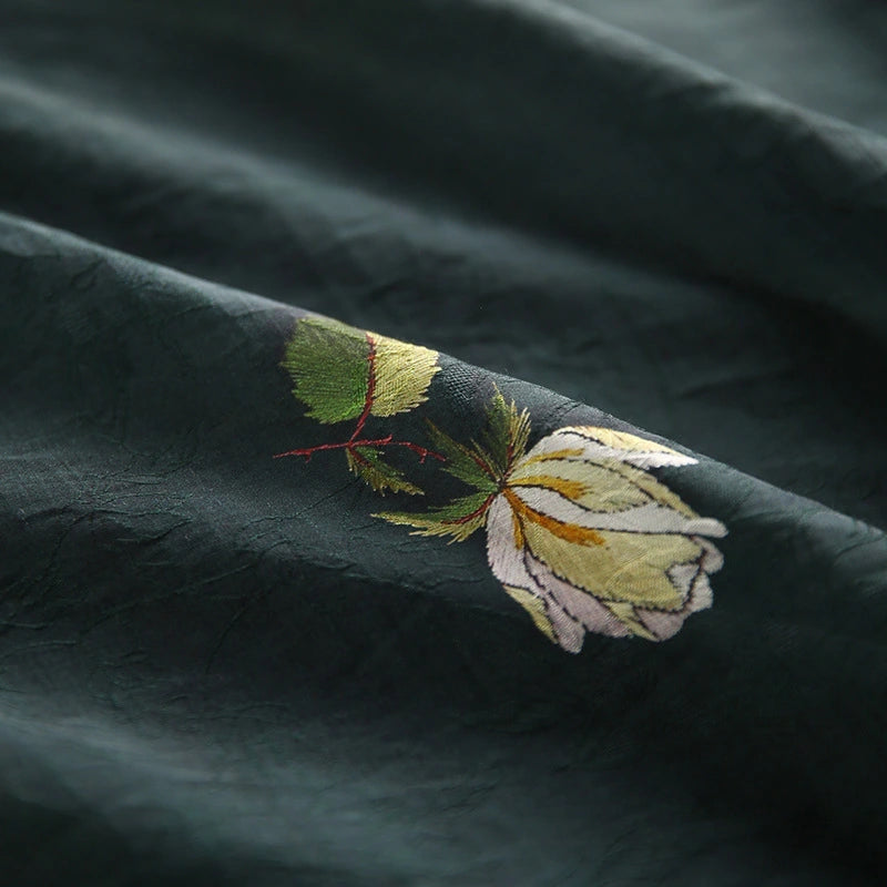 Close-up of Longan Craft's Rose Printed Lyocell Fabric, featuring botanical embroidery with a pale yellow flower and green leaves, highlighting detailed stitching on soft, slightly textured lyocell material for dressmaking.