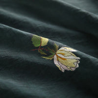 Close-up of Longan Craft's Rose Printed Lyocell Fabric, featuring botanical embroidery with a pale yellow flower and green leaves, highlighting detailed stitching on soft, slightly textured lyocell material for dressmaking.
