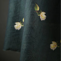 A close-up of Longan Craft's Rose Printed Lyocell Fabric shows botanical embroidery of yellow roses and green leaves on breathable lyocell textile, partially draped against a dark background—ideal for dressmaking by the yard.
