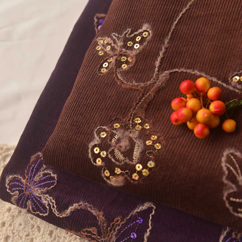Close-up of Longan Craft’s Sequined Floral Embroidered Corduroy Fabric by the Yard—fine wale cotton corduroy featuring floral and butterfly sequin designs, accented with a bunch of orange and red artificial berries.