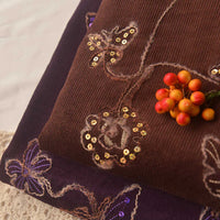 Close-up of Longan Craft’s Sequined Floral Embroidered Corduroy Fabric by the Yard—fine wale cotton corduroy featuring floral and butterfly sequin designs, accented with a bunch of orange and red artificial berries.
