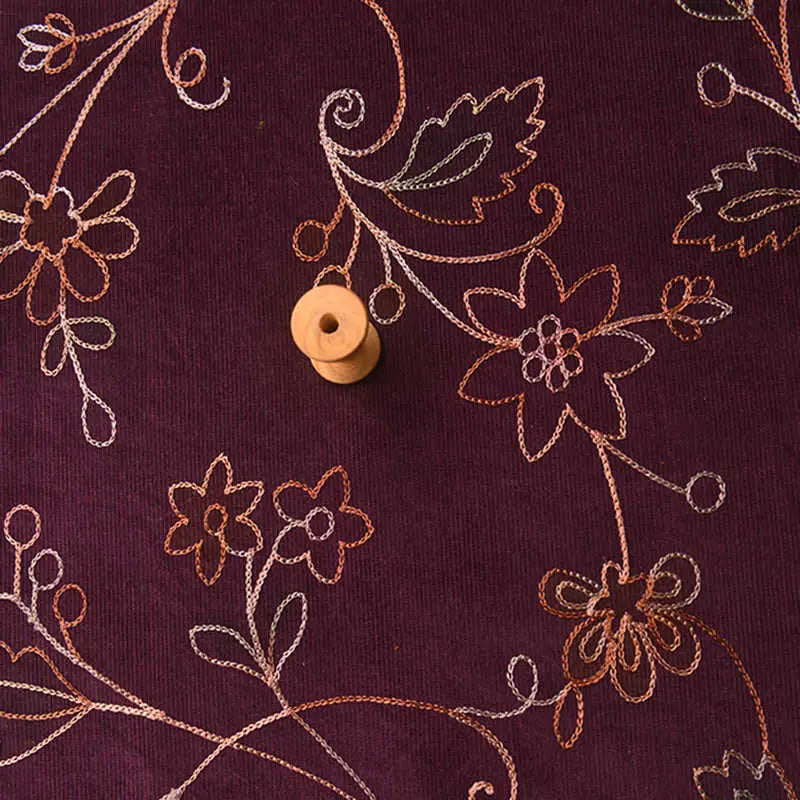 A small wooden spool rests on Longan Craft’s Sequined Floral Embroidered Corduroy Fabric, featuring fine wale cotton with orange, pink, and white floral patterns—perfect DIY material by the yard for sewing projects.
