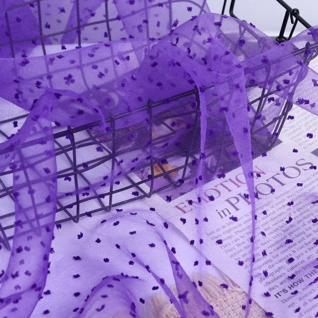 Sheer purple Swiss Dot Organza Fabric By The Yard draped over a wire basket.