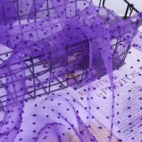Sheer purple Swiss Dot Organza Fabric By The Yard draped over a wire basket.