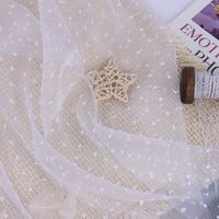 Sheer Swiss Dot Organza Fabric By The Yard draped over a woven mat with a star-shaped ornament.
