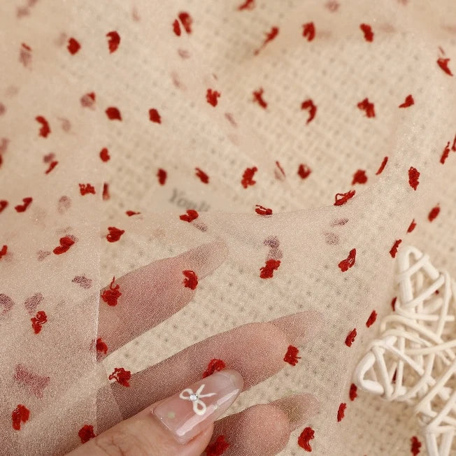 Sheer beige Swiss dot organza fabric by the yard featuring small, raised red dots.
