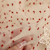 Sheer beige Swiss dot organza fabric by the yard featuring small, raised red dots.