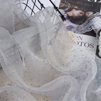 Sheer, white Sheer Swiss Dot Organza Fabric By The Yard with small, raised polka dots draped over a magazine.