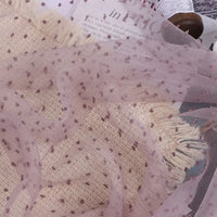Sheer, light purple Sheer Swiss Dot Organza Fabric By The Yard with raised, darker purple polka dots draped over a piece of textured, cream-colored fabric.