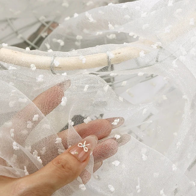A hand holds up Longan Craft Sheer Swiss Dot Organza Fabric, a lightweight sheer material decorated with small, raised white dots.