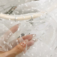 A hand holds up Longan Craft Sheer Swiss Dot Organza Fabric, a lightweight sheer material decorated with small, raised white dots.