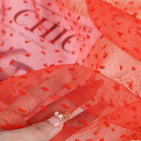 A hand holding a piece of Sheer Swiss Dot Organza Fabric By The Yard featuring sheer fabric with textured red 3D dots.