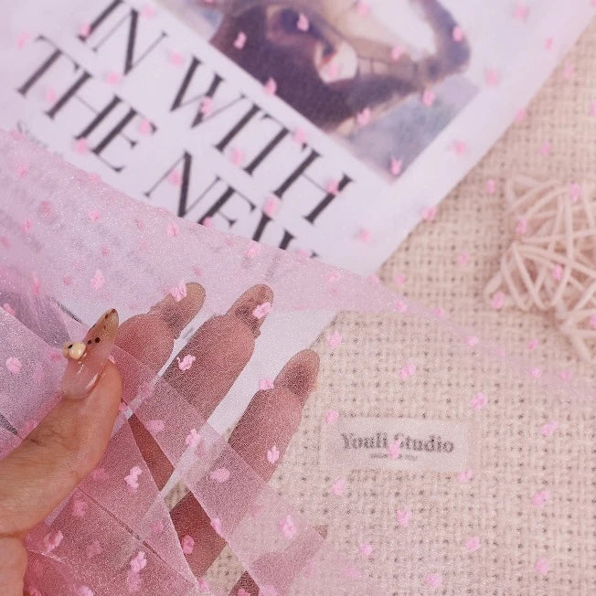 A hand holds a piece of Sheer Swiss Dot Organza Fabric By The Yard, featuring delicate 3D flower-shaped accents.
