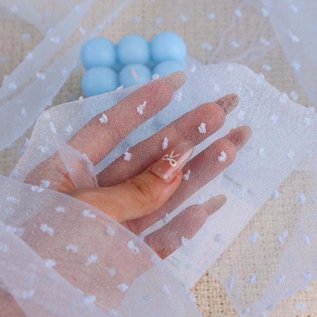 A hand holds up a piece of Longan Craft Sheer Swiss Dot Organza Fabric By The Yard, which is a sheer material featuring raised, colorful 3D dots.
