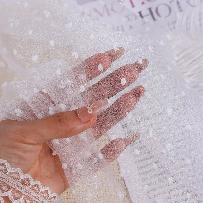 A hand holds up a piece of Sheer Swiss Dot Organza Fabric By The Yard, which is a sheer material covered in small, raised 3D dots.