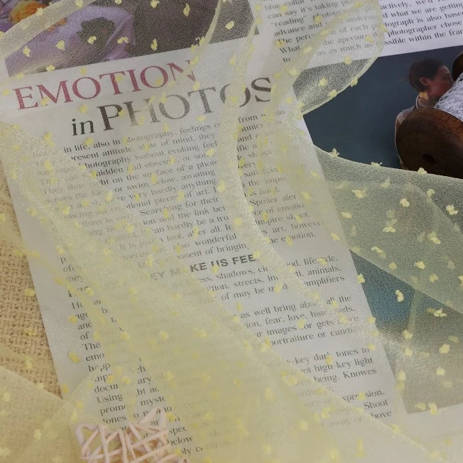 Sheer yellow Longan Craft Sheer Swiss Dot Organza Fabric By The Yard with small, raised 3D dots, draped over a printed book page.
