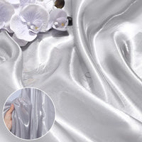Close-up of Longan Craft’s Shiny Liquid Organza Fabric By The Yard—colorful, glossy finish luxury textile—with delicate white and purple artificial orchids on top. Inset: hand holding this reflective organza gown material.