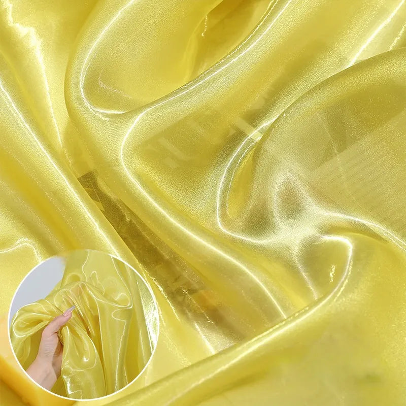 Shiny Liquid Organza Fabric by Longan Craft is draped in soft folds, its sheer yellow luxury gown material catching the light. An inset highlights a hand gathering this lightweight, glossy textile to show off its texture and sheen.
