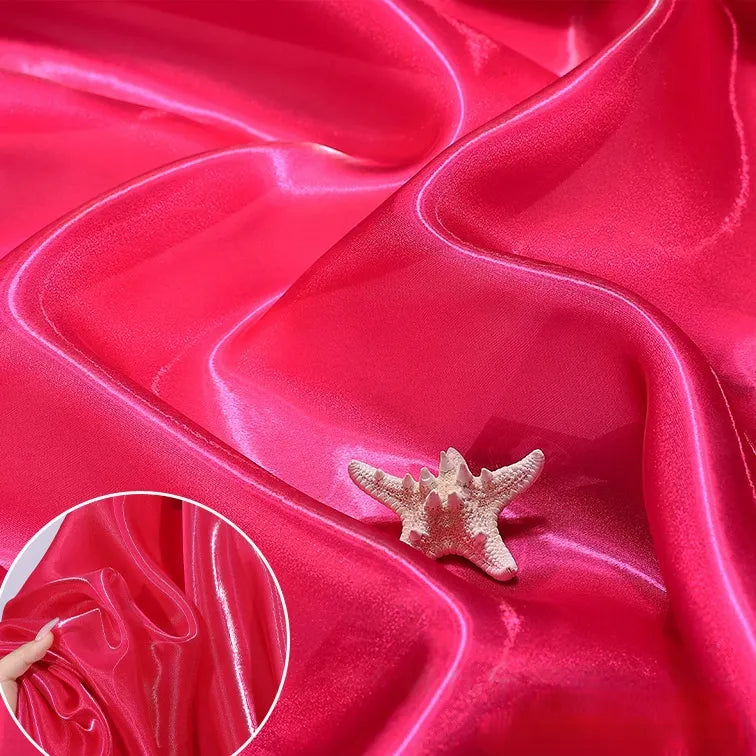The vibrant Shiny Liquid Organza Fabric By The Yard from Longan Craft features a glossy, colorful finish draped in folds with a starfish accent. An inset shows its smooth texture, ideal for luxury gowns and evening wear.