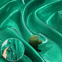 Shiny Liquid Organza Fabric by Longan Craft features a colorful, glossy finish with a smooth, reflective surface and gentle folds; inset shows a hand holding the luxury organza gown material to highlight its texture and sheen.